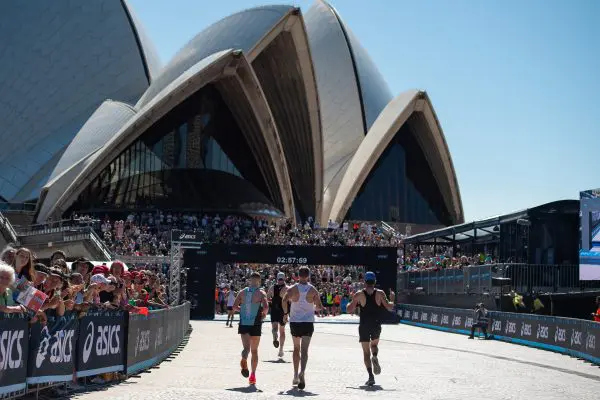 Groupe de coureurs à quelques mètres de la ligne d'arrivée du Marathon de Sydney, à l'ombre de l'emblématique Opéra de Sydney.